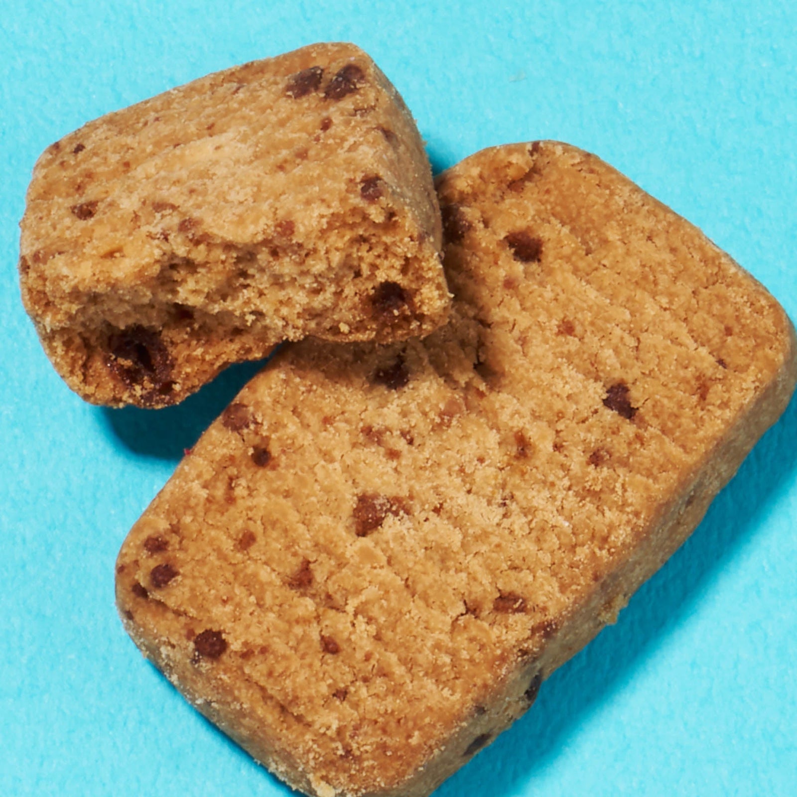 Two rectangular chocolate chip cookies, one partially broken, are showcased on a bright blue background, reminiscent of the tasty finds in the Bokksu Snack Box: Seasons of Japan.